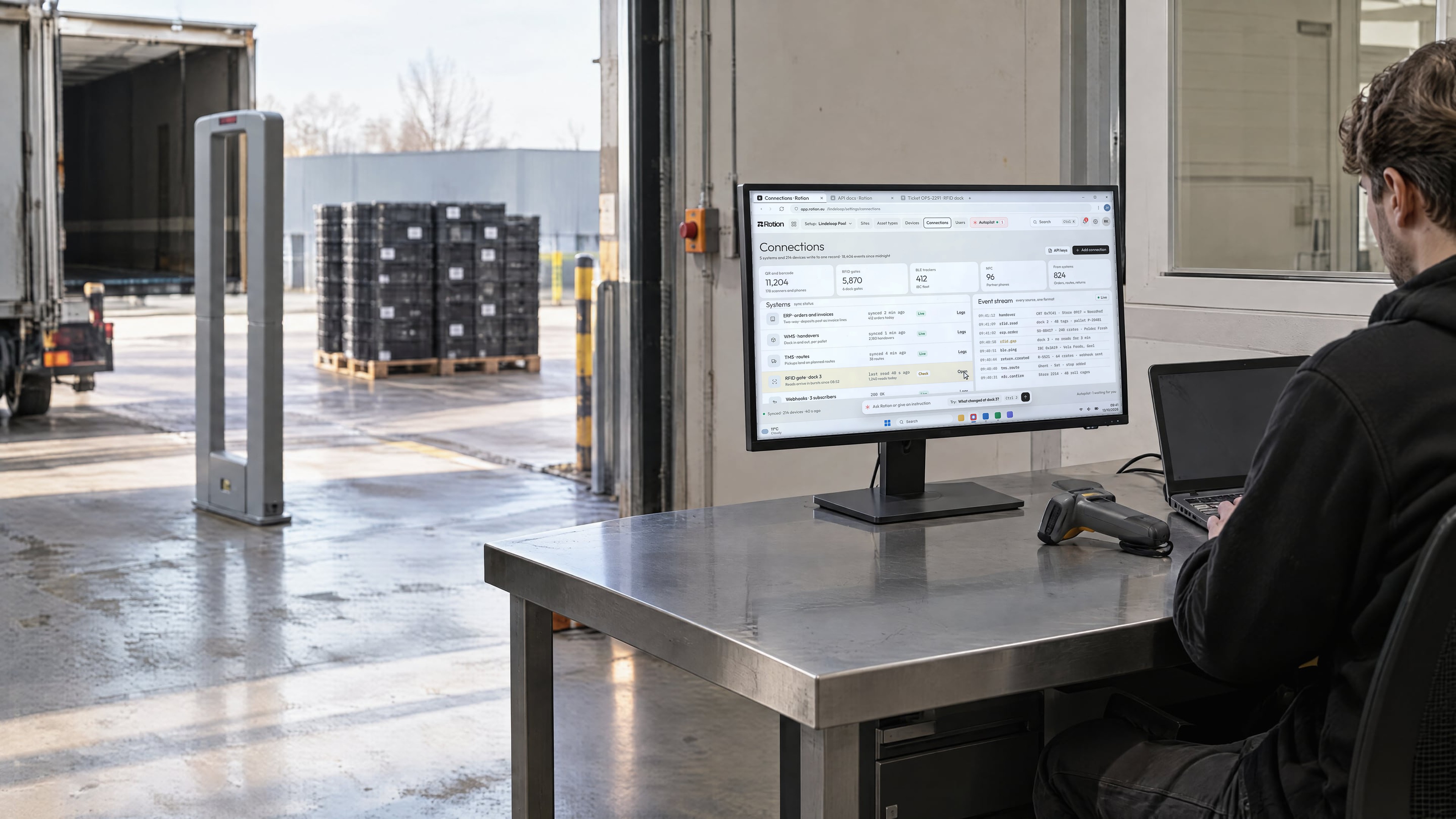 An engineer at a steel desk beside a loading dock, the monitor showing Rotion connections and a live event stream from scanners, RFID gates and systems