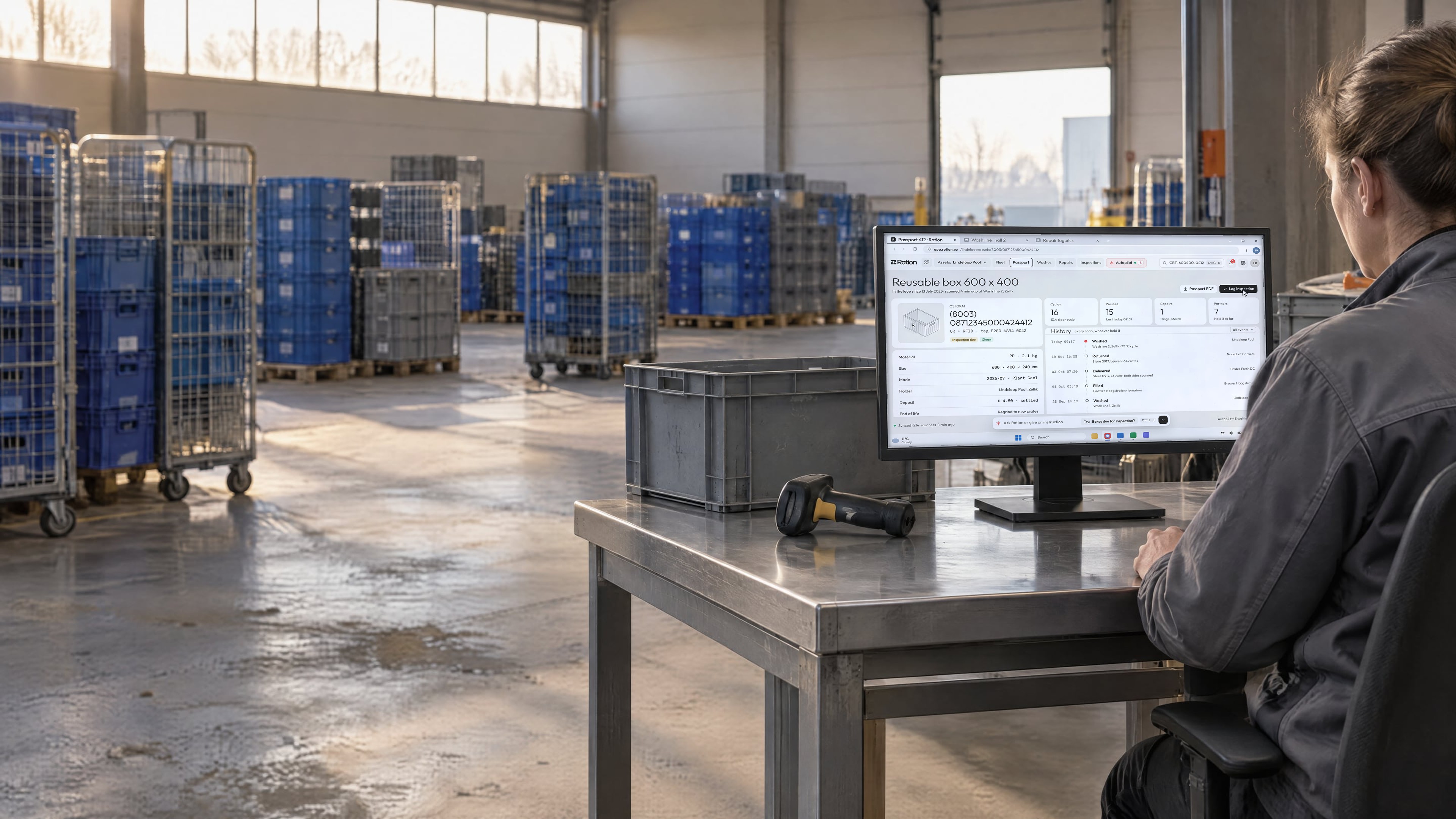 A supervisor at a steel workstation on the warehouse floor, the monitor showing the passport of one reusable box with its cycles, washes and history