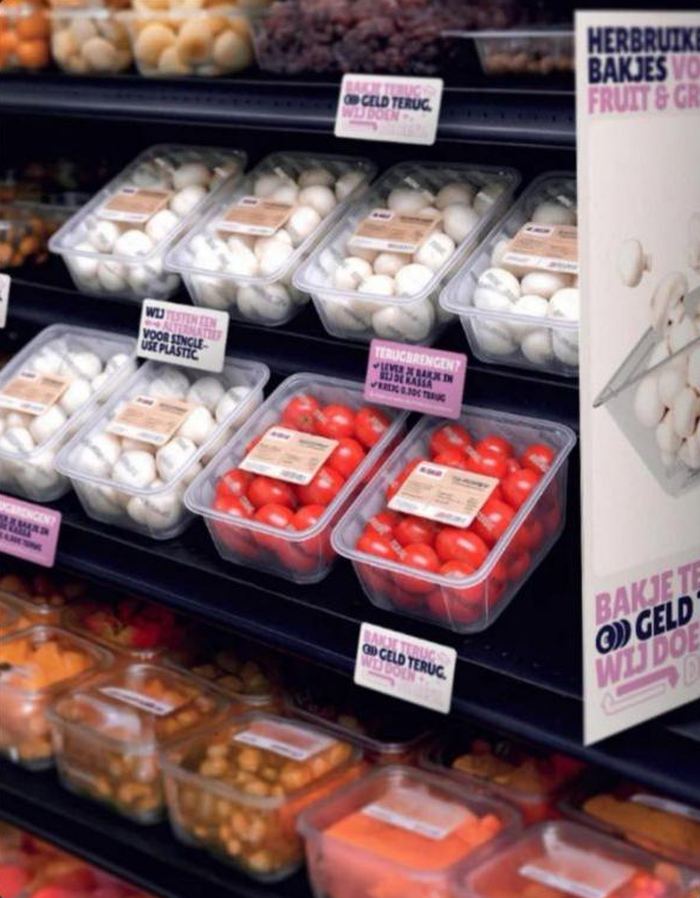 Herbruikbare schalen met witte champignons en kerstomaten in een supermarktrek, met statiegeldlabels op de rand van het schap